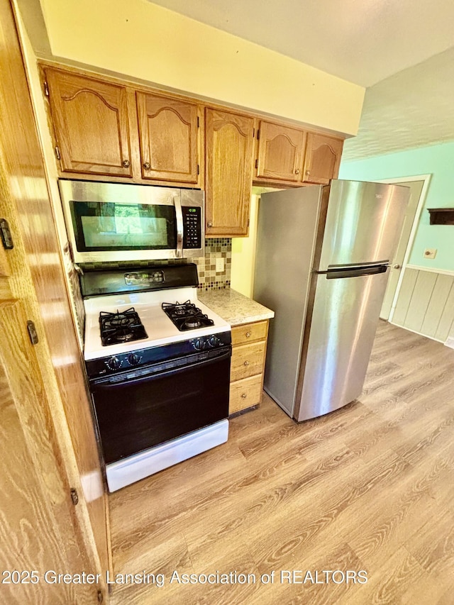 1214 Otto Rd Unit R1, Charlotte, MI 48813 - kitchen with appliances with stainless steel finishes, light wood-style floors, light countertops, a wainscoted wall, and backsplash
