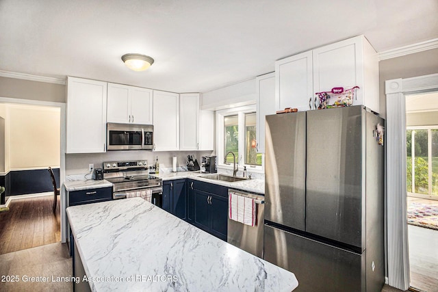 4326 Manitou Dr, Okemos, MI 48864 - kitchen featuring appliances with stainless steel finishes, white cabinets, ornamental molding, light stone counters, and wood finished floors