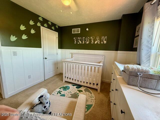 310 Brittany Ln, Mulliken, MI 48861 - bedroom with a wainscoted wall, light colored carpet, a crib, and a ceiling fan