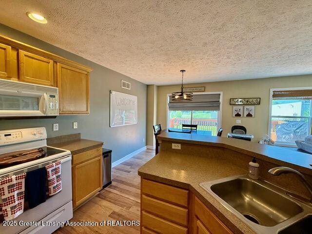 310 Brittany Ln, Mulliken, MI 48861 - kitchen featuring white appliances, a textured ceiling, healthy amount of natural light, light wood-style floors, and hanging light fixtures