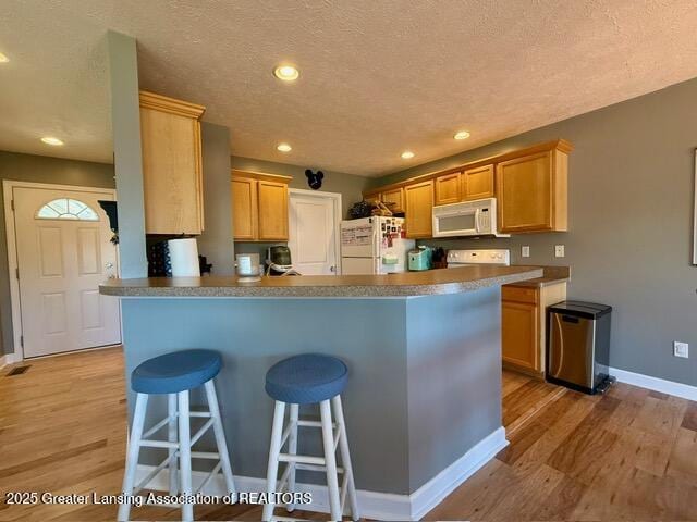 310 Brittany Ln, Mulliken, MI 48861 - kitchen with white appliances, light wood-style flooring, a breakfast bar area, a textured ceiling, and a peninsula
