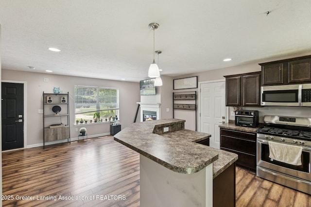 4930 N Campers Trl, Perrinton, MI 48871 - kitchen with stainless steel appliances, a kitchen island, a glass covered fireplace, wood finished floors, and dark countertops