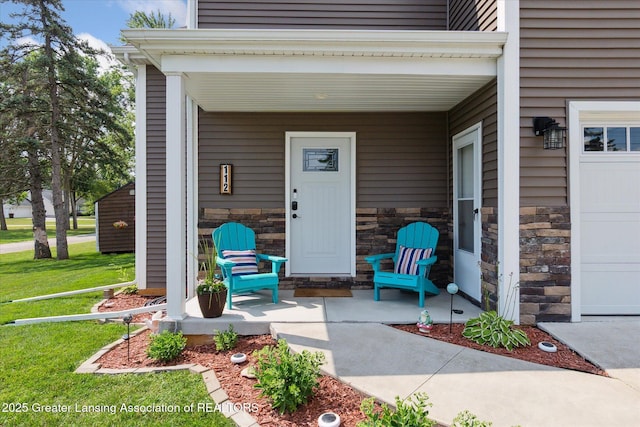 112 E Barber St, Ithaca, MI 48847 - property entrance with covered porch, stone siding, a yard, and a garage