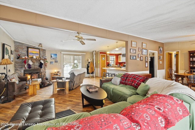 9428 S Wright Rd, Eagle, MI 48822 - living room featuring ornamental molding, a textured ceiling, wood finished floors, ceiling fan, and a stone fireplace