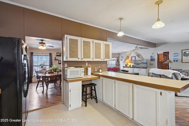 9428 S Wright Rd, Eagle, MI 48822 - kitchen with black refrigerator with ice dispenser, a ceiling fan, white microwave, ornamental molding, and a peninsula