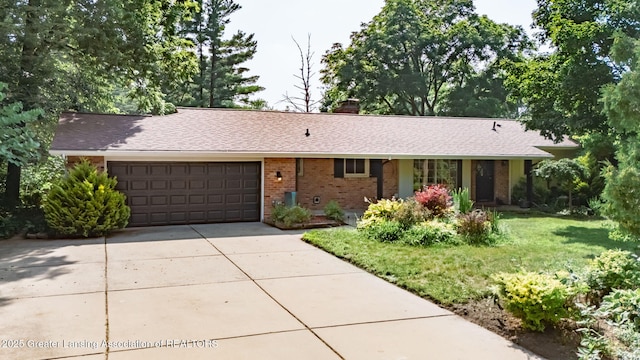 2315 Hamilton Rd, Okemos, MI 48864 - ranch-style home featuring brick siding, a chimney, an attached garage, a shingled roof, and concrete driveway