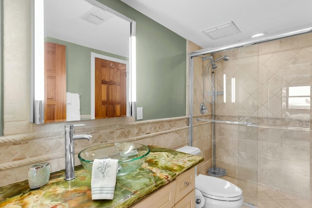 bathroom with visible vents, toilet, tile walls, a shower stall, and vanity