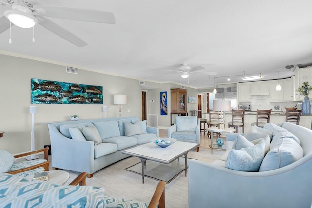 living room featuring light wood finished floors, ornamental molding, a ceiling fan, and visible vents