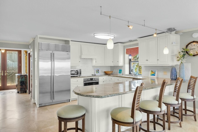 kitchen featuring a peninsula, ornamental molding, light stone countertops, and stainless steel appliances