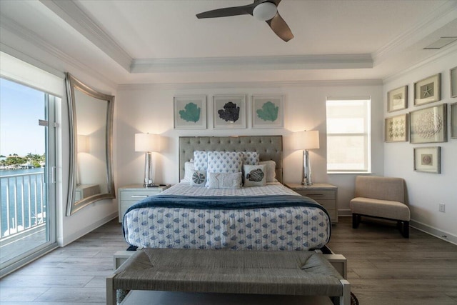bedroom with a tray ceiling, access to exterior, wood finished floors, and ornamental molding