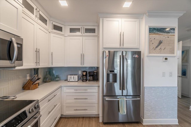 kitchen with light countertops, white cabinetry, stainless steel appliances, light wood-style floors, and decorative backsplash