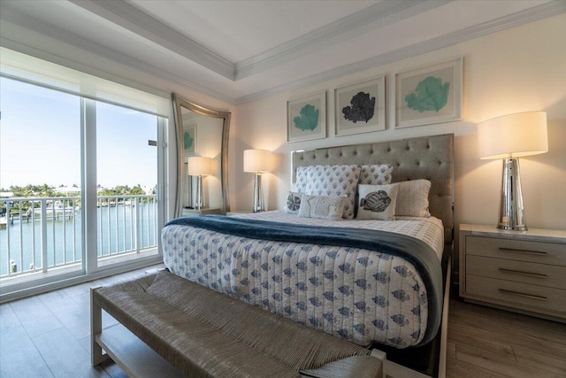 bedroom with a water view, ornamental molding, access to outside, wood finished floors, and a raised ceiling