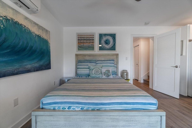 bedroom featuring a wall mounted air conditioner, baseboards, and wood finished floors