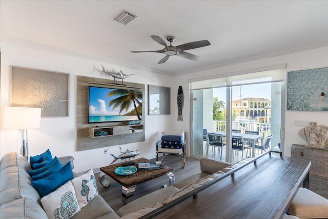 living area with wood finished floors, visible vents, ornamental molding, and ceiling fan