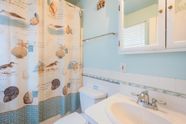 bathroom featuring a shower with shower curtain, toilet, a sink, wainscoting, and tile walls