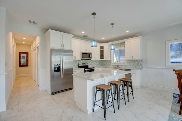 kitchen with a kitchen bar, marble finish floor, a wainscoted wall, white cabinets, and appliances with stainless steel finishes