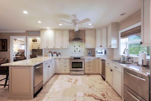 kitchen with appliances with stainless steel finishes, wall chimney range hood, ceiling fan, a sink, and a peninsula