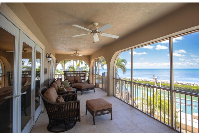 sunroom featuring a water view, tile patterned floors, outdoor lounge area, a ceiling fan, and a textured ceiling