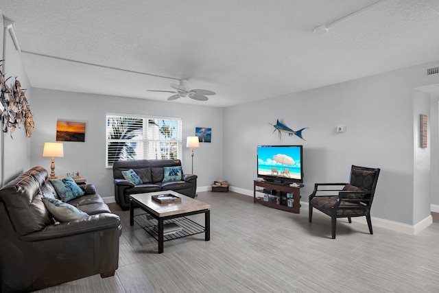 living room with a textured ceiling, light wood-type flooring, a ceiling fan, and baseboards