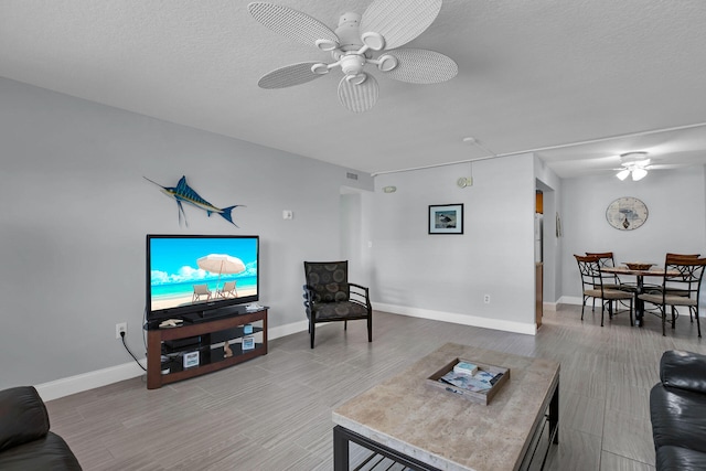 living room featuring a textured ceiling, baseboards, a ceiling fan, and wood finished floors