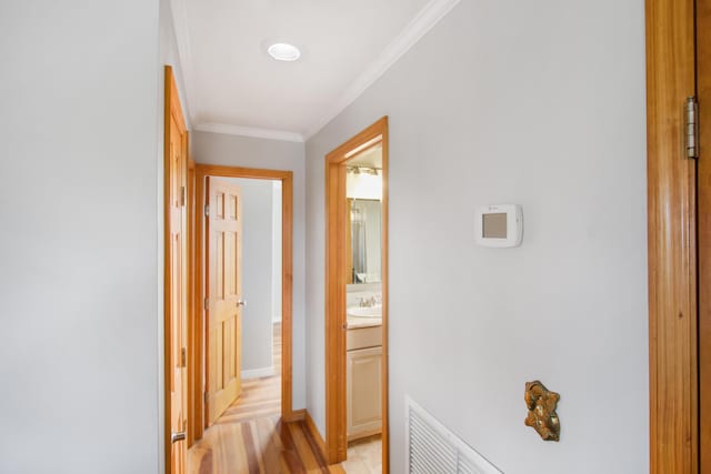 corridor featuring visible vents, ornamental molding, light wood-style floors, a sink, and baseboards