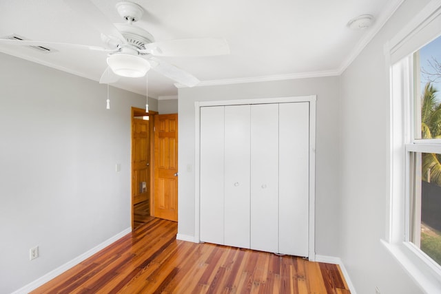 unfurnished bedroom with a closet, crown molding, baseboards, and wood finished floors