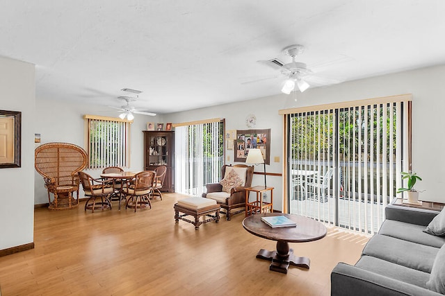 living room with baseboards, visible vents, wood finished floors, and a ceiling fan