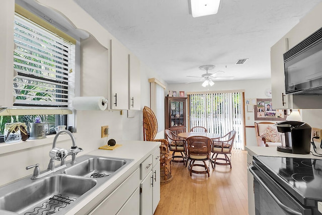kitchen with white cabinets, visible vents, light wood-style flooring, a sink, and black appliances