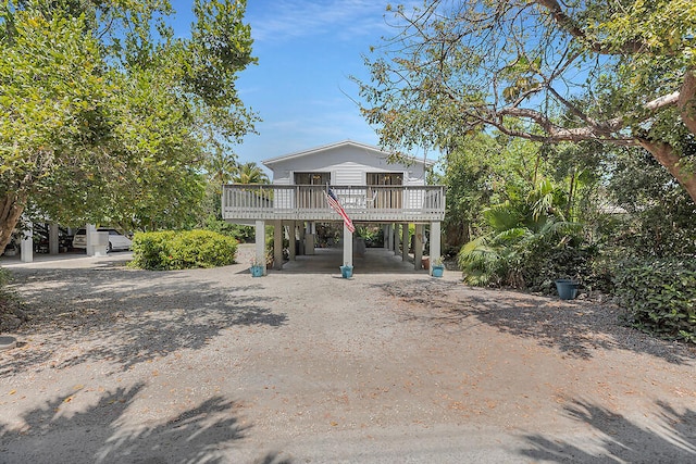 coastal home with dirt driveway, a wooden deck, and a carport