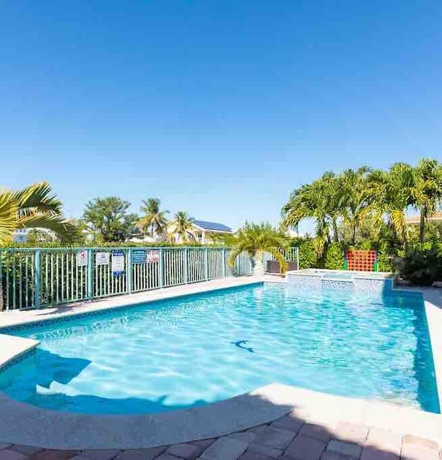 view of swimming pool featuring a pool with connected hot tub and fence