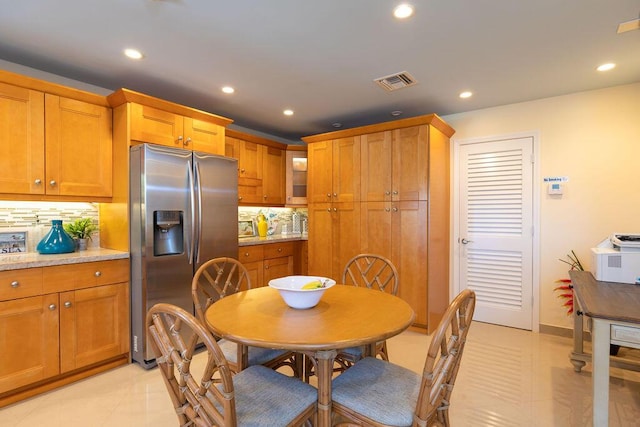 kitchen with light tile patterned floors, stainless steel fridge, visible vents, brown cabinets, and backsplash