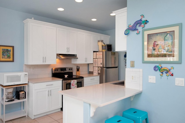 461 3rd St, Key Colony, FL 33051 - kitchen featuring appliances with stainless steel finishes, under cabinet range hood, a breakfast bar area, tasteful backsplash, and white cabinets