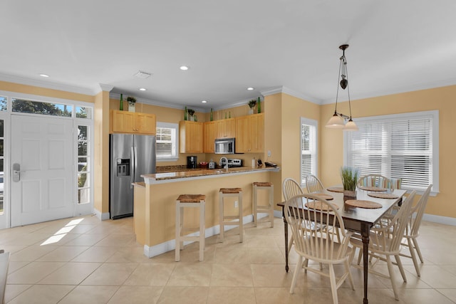 kitchen featuring decorative light fixtures, stainless steel appliances, light tile patterned flooring, light brown cabinets, and a peninsula