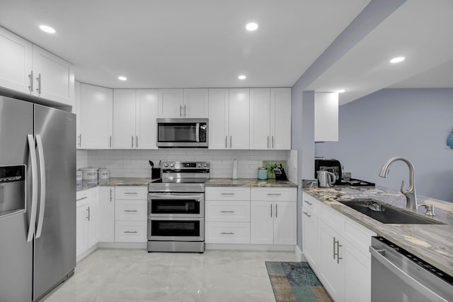 kitchen with white cabinets, decorative backsplash, light stone countertops, stainless steel appliances, and a sink