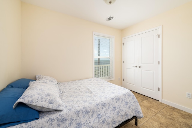 bedroom with light tile patterned floors, visible vents, baseboards, and a closet