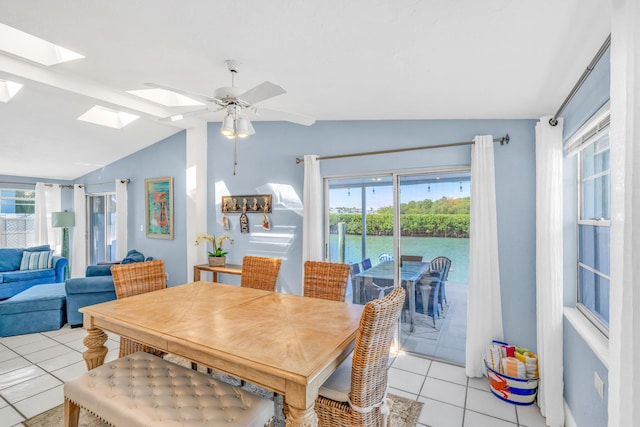 dining space featuring a ceiling fan, lofted ceiling with skylight, plenty of natural light, and light tile patterned flooring
