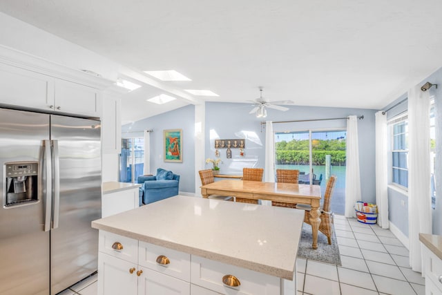kitchen with light tile patterned floors, vaulted ceiling with skylight, white cabinets, stainless steel fridge, and a center island