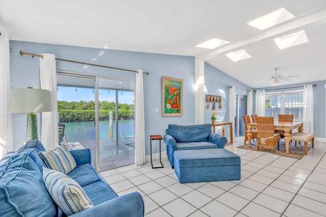 living room featuring lofted ceiling with skylight, a water view, a ceiling fan, light tile patterned floors, and baseboards
