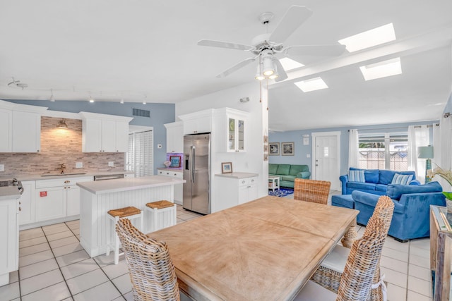 dining space with lofted ceiling with skylight, light tile patterned floors, a ceiling fan, and visible vents