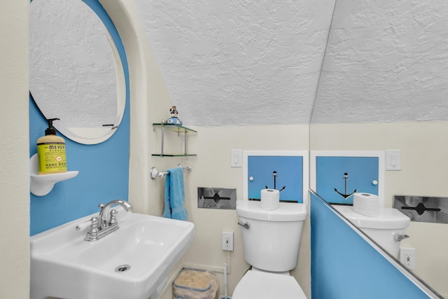 bathroom with vaulted ceiling, toilet, a sink, and a textured ceiling