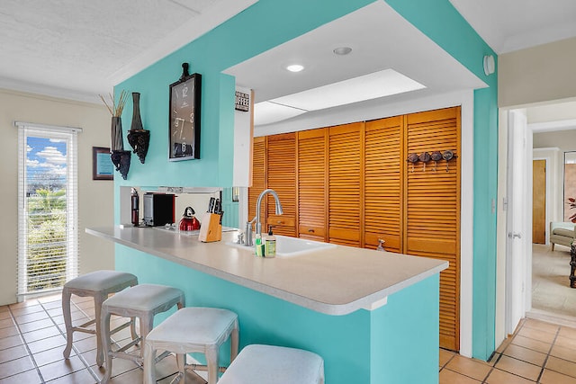kitchen featuring light tile patterned flooring, crown molding, light countertops, a sink, and a kitchen bar