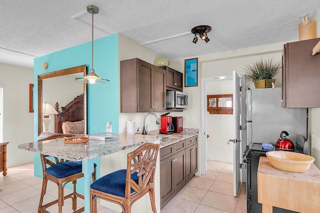 kitchen featuring stainless steel microwave, a sink, light tile patterned flooring, light stone counters, and dark brown cabinets