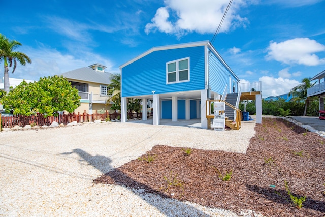 view of front of house featuring a carport, gravel driveway, fence, and stairs