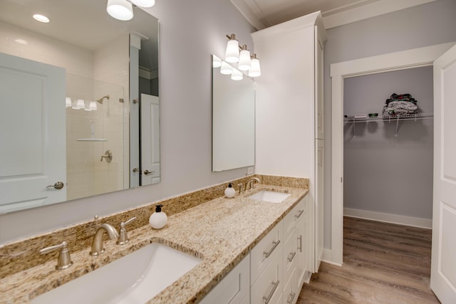 full bathroom featuring a stall shower, a walk in closet, a sink, and wood finished floors