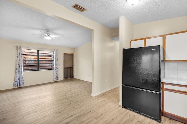 kitchen with visible vents, tile counters, freestanding refrigerator, light wood-type flooring, and white cabinetry