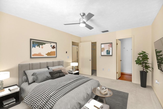 bedroom featuring visible vents, a spacious closet, a ceiling fan, light carpet, and a textured ceiling