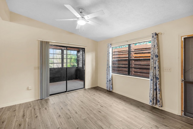 empty room with a textured ceiling, light wood-type flooring, lofted ceiling, and a ceiling fan