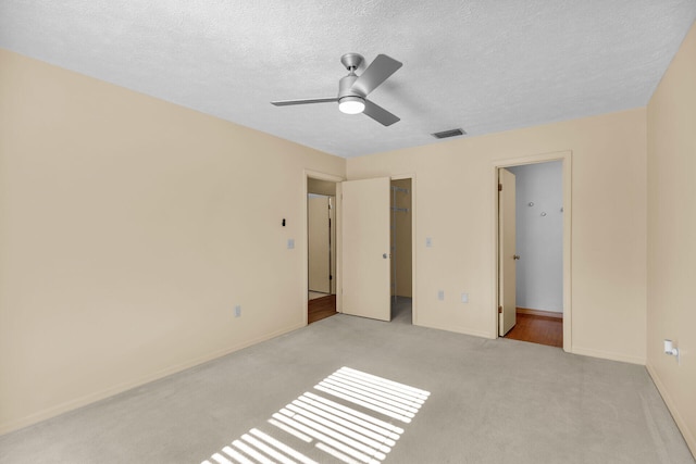 unfurnished bedroom featuring baseboards, visible vents, light colored carpet, a spacious closet, and a textured ceiling