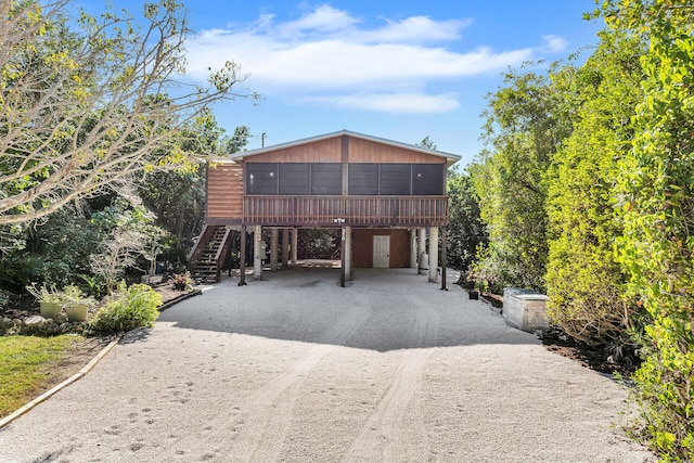 view of front of property featuring a carport, a sunroom, dirt driveway, and stairs