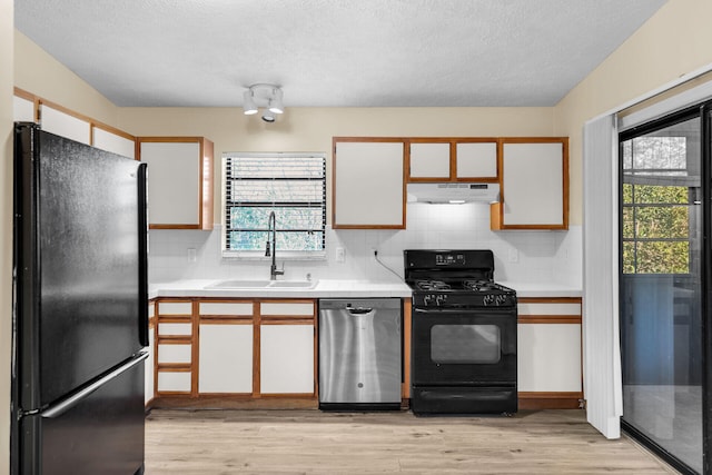 kitchen with white cabinets, under cabinet range hood, light countertops, black appliances, and a sink